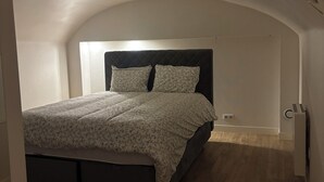 Et soveværelse med seng, sengegavl, radiator og trægulv.