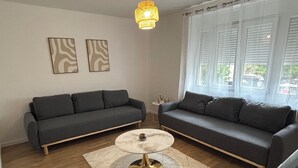En stue med to mørkegrå sofaer, et rundt sofabord med gylden fod, og et tæppe med et mønster. Der hænger en lampe over sofabordet.