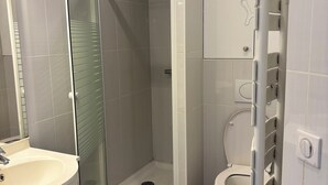 Et moderne badeværelse med en glasafskærmet brusekabine, toilet og håndvask med spejl.