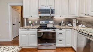 Cucina con mobili bianchi, elettrodomestici in acciaio inossidabile e piano di lavoro in granito.
