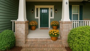Una casa con una porta verde, due vasi di fiori davanti al portone e un portico con colonne bianche.