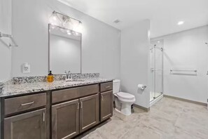 A modern bathroom with a granite countertop, a large mirror, a toilet, and a glass-enclosed shower. - DT · Fast Wifi · Pet Friendly · Bidet Sprayer (Cleveland)