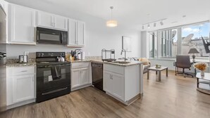 A modern kitchen with white cabinets, a built-in microwave, a stove, and a dishwasher. There is a small island with a sink and a dining area with a table and chairs. - DT · Fast Wifi · Pet Friendly · Bidet Sprayer (Cleveland)