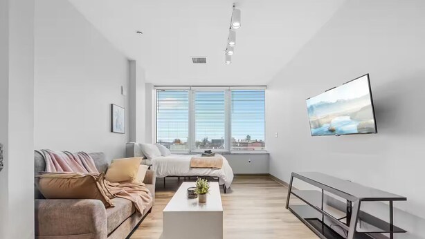 A modern living room with a sofa, a coffee table, and a TV mounted on the wall. - DT · Gym · Pet Friendly · 1 Bus to Clinic or CSU (Cleveland)