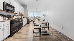A modern kitchen with white cabinets, a built-in oven, and a microwave. There is a dining area with a wooden table and chairs. - DT · Gym · Pet Friendly · 1 Bus to Clinic or CSU (Cleveland)
