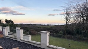 An outdoor seating area with a view of a grassy field and distant landscape. - Caledfryn (Tyn-y-Gongl)