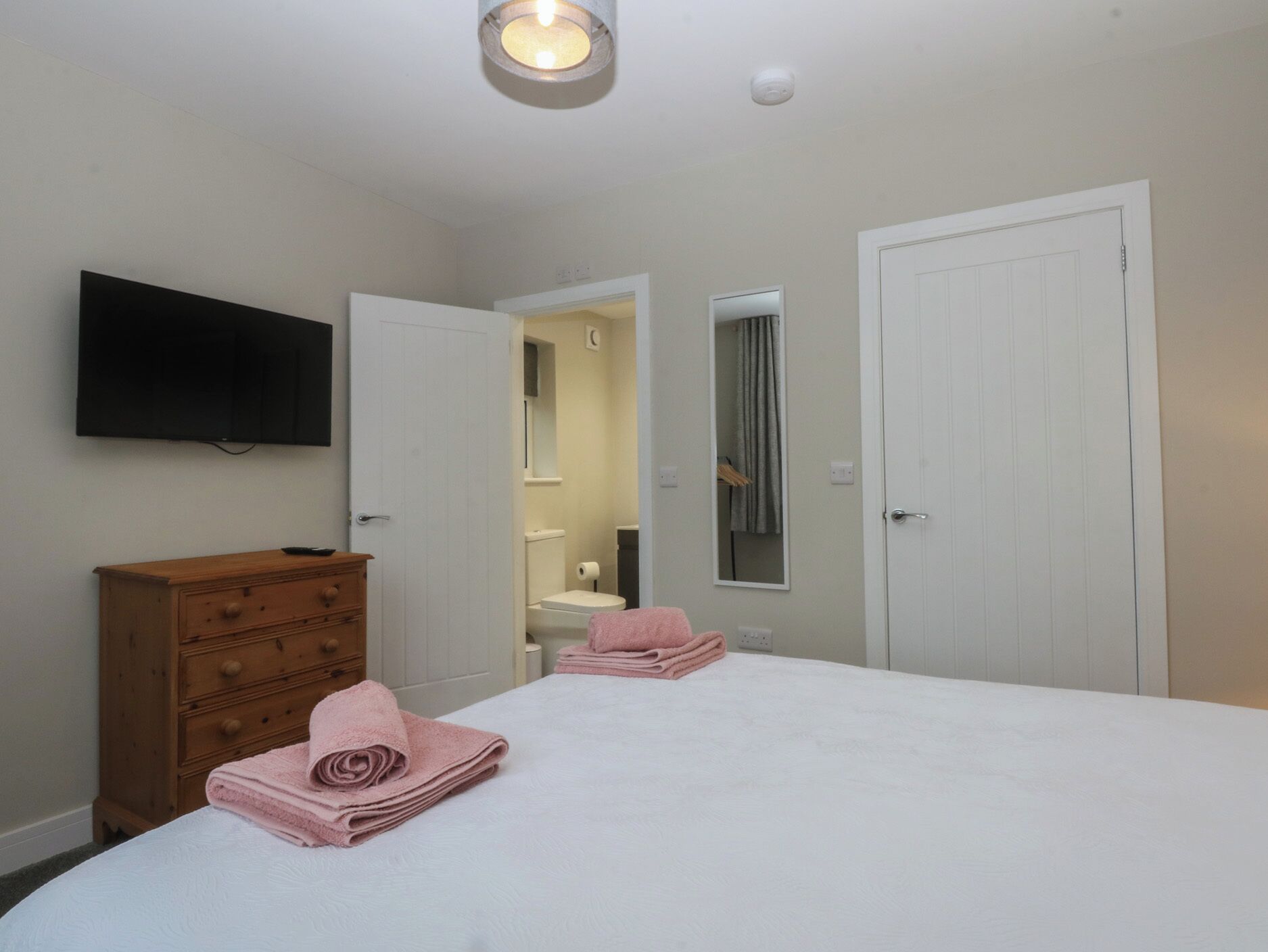 Une chambre à coucher avec un lit, une commode, un téléviseur et une salle de bain visible à travers une porte ouverte.