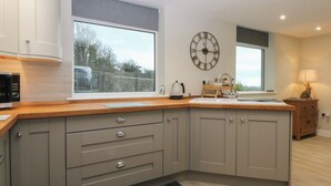 A modern kitchen with grey cabinetry, a wooden countertop, a built-in sink, and a large window. - Caledfryn (Tyn-y-Gongl)
