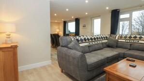 A modern living room with a sectional sofa, a wooden coffee table, and a lamp on a side table. - Caledfryn (Tyn-y-Gongl)