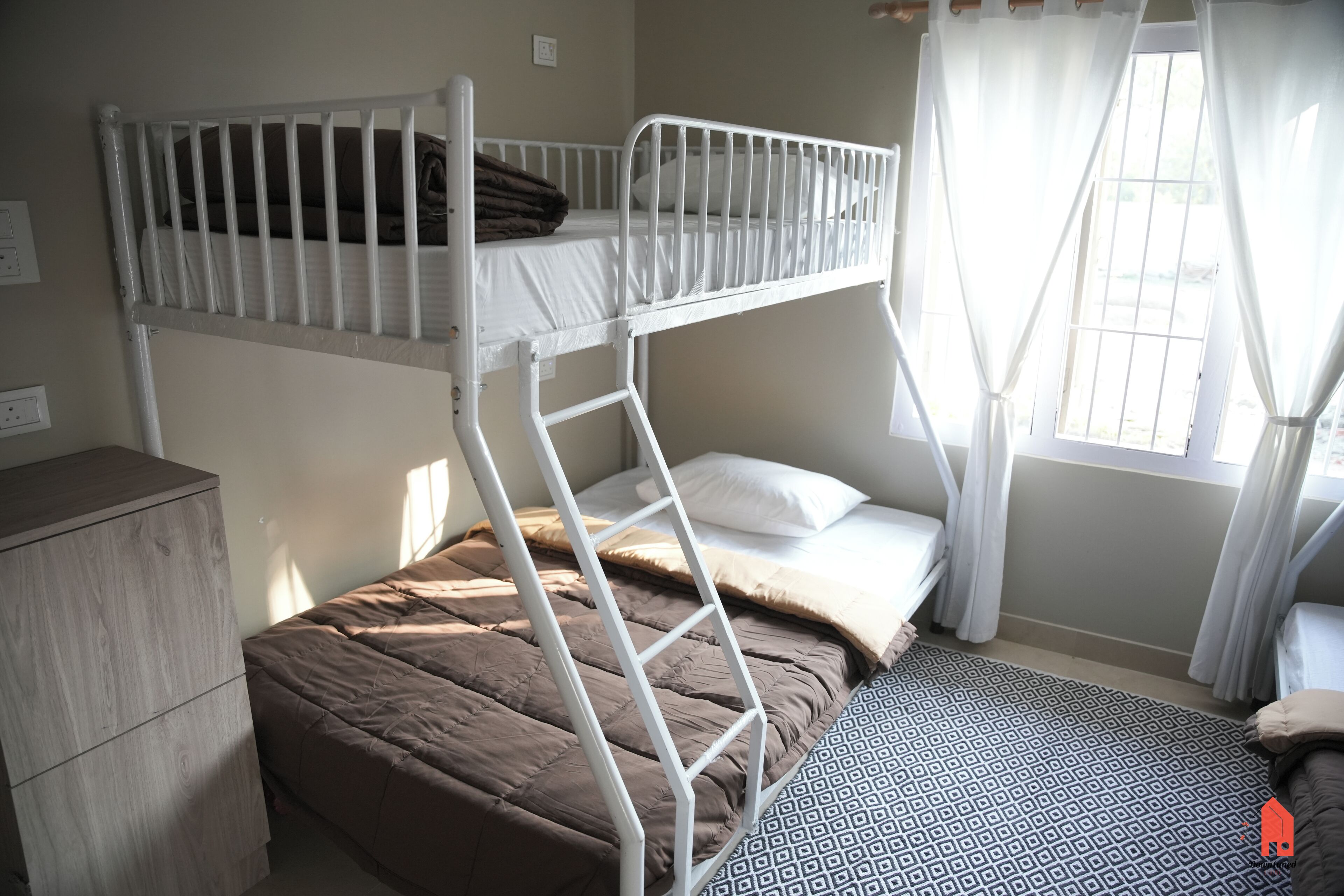 A bunk bed room with a ladder, a bedside table, and a window with curtains.
