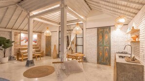 Una habitación amplia con techo alto, paredes de ladrillo visto y techo de madera rústica. Hay una hamaca, una mesa de madera y un sofá.