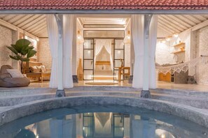 Un área de spa con un jacuzzi, una cama con dosel y una zona de estar con una planta.