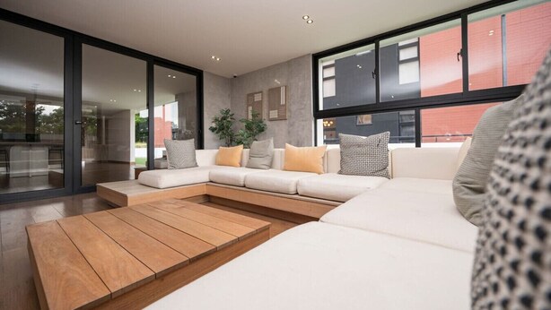 Ein modernes Wohnzimmer mit einer Eckcouch, einem Holztisch und großen Fenstern mit Blick nach draußen.