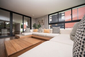 Ein modernes Wohnzimmer mit einer Eckcouch, einem Holztisch und großen Fenstern mit Blick nach draußen.
