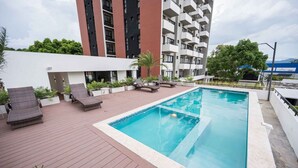 Ein Pool auf dem Dach mit Liegestühlen und Blick auf ein Hochhaus.