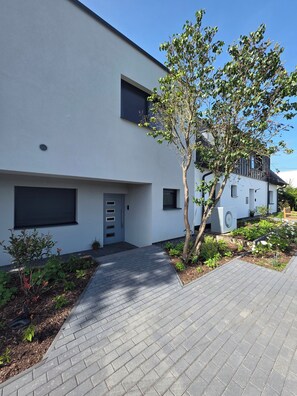 A modern two-story building with a paved driveway, a small garden area, and a tree. - Panoramic Views and Comfort: "Weitblick" Vacation Rental   (Nümbrecht)