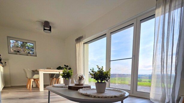 Ein modernes Wohnzimmer mit einem runden Couchtisch, einer gepolsterten Sitzecke und Blick auf die Landschaft durch große Fenster.