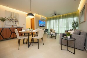 A modern living room with a dining area, a grey sofa, a TV, and a ceiling fan. - Accommodates 15 Guests | 2 Full Apartments in the Same Building (Santiago de los Caballeros)