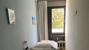 Una stanza piccola e stretta con un letto, una finestra e uno sgabello.