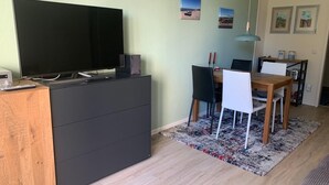 Un soggiorno moderno con una TV a schermo piatto su un mobile nero, una zona pranzo con tavolo e sedie in legno, e un tappeto decorato.