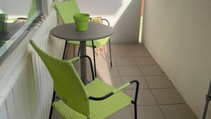 Un piccolo balcone con un tavolino rotondo e due sedie, una con cuscino verde.
