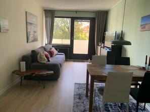 Un salon comprenant un canapé, une table à manger, des chaises, une lampe et une vue dégagée sur l’extérieur grâce à une grande fenêtre.