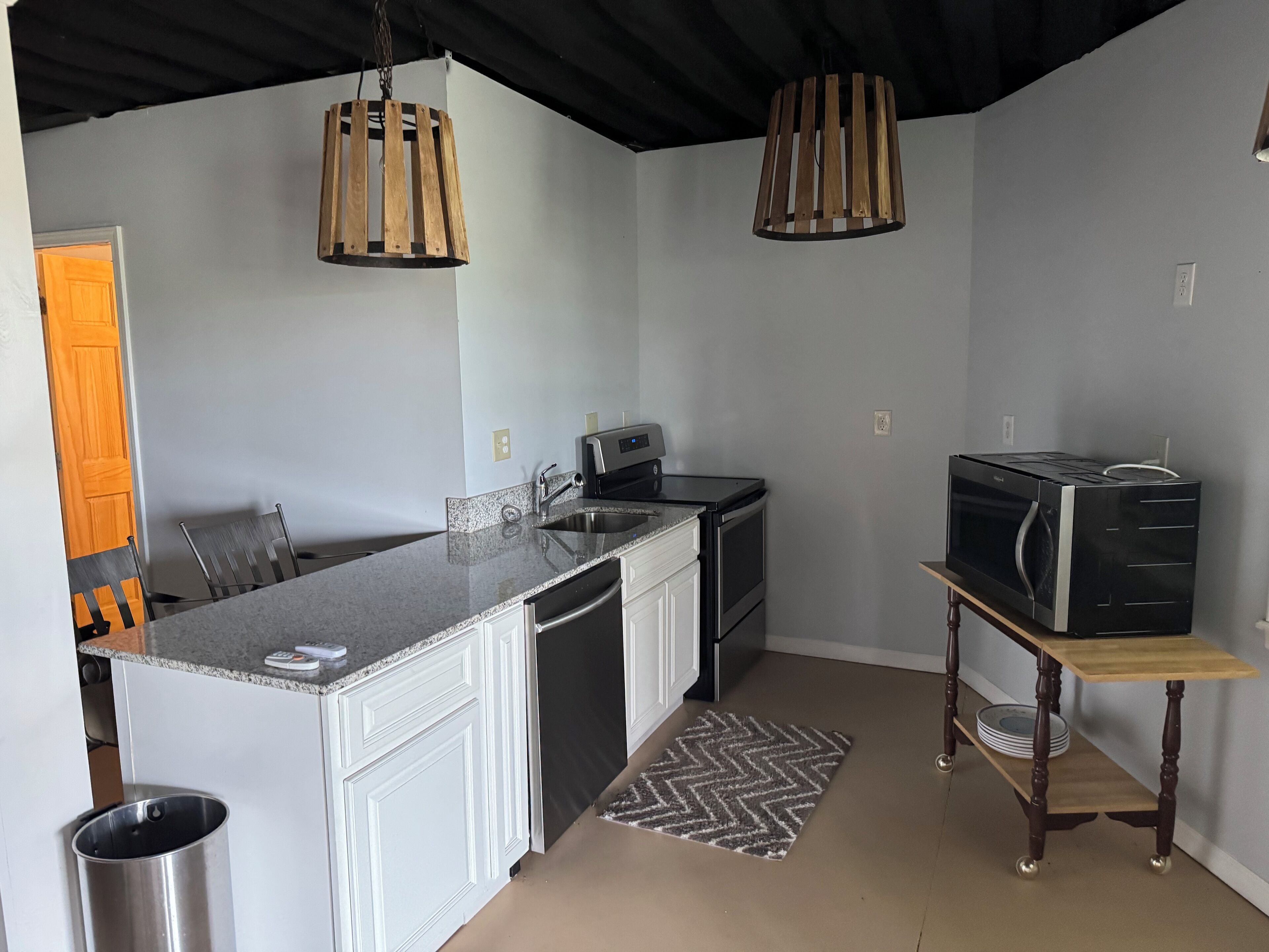 A compact kitchen with a granite countertop, stainless steel appliances, and a wooden hanging light fixture.