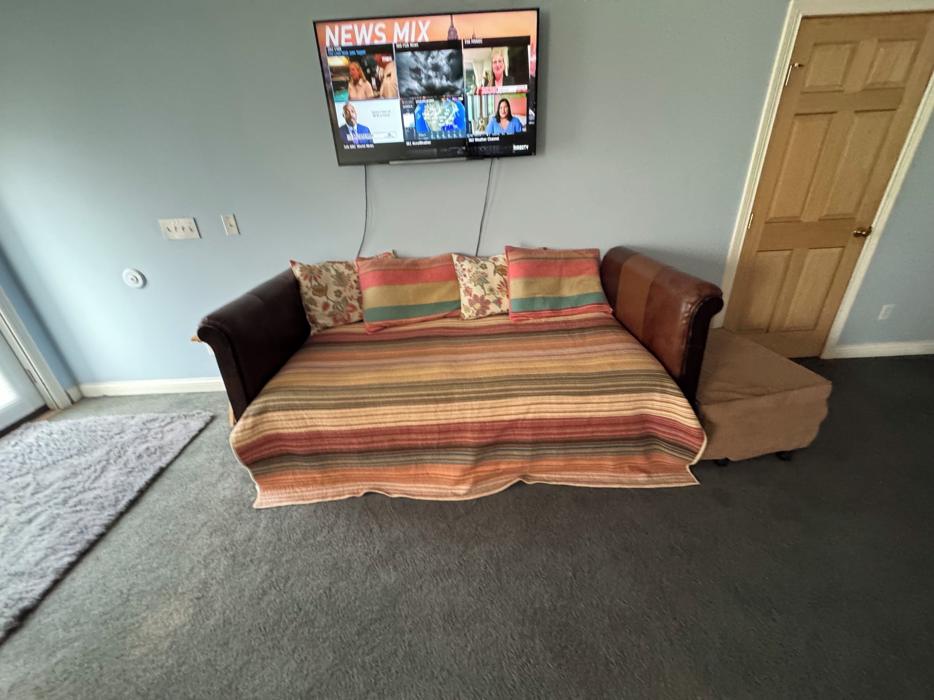 A room with a large bed, a television mounted on the wall displaying news, and a wooden door.