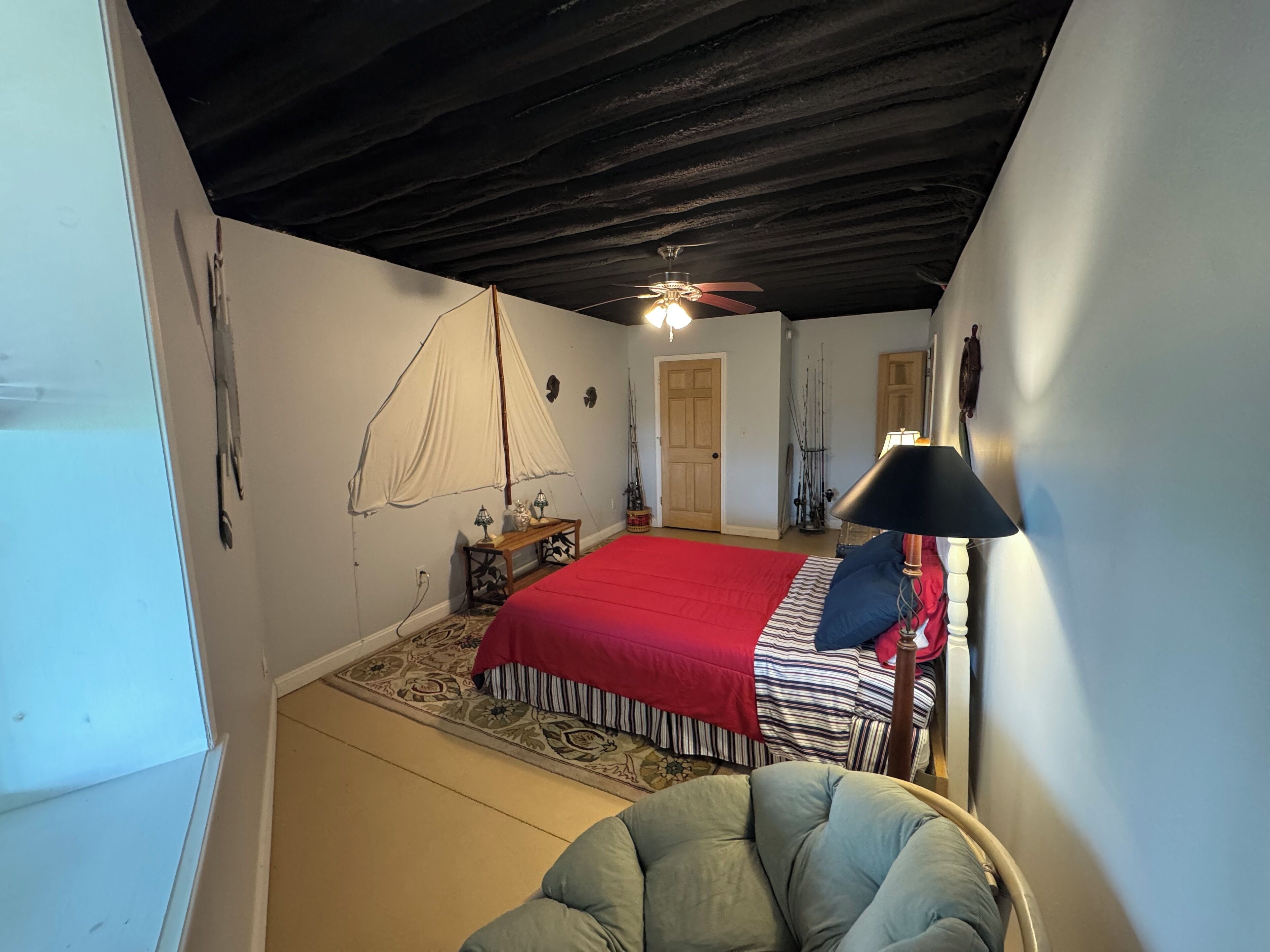 A bedroom with a bed, a ceiling fan, a lamp, and fishing rods against the wall.