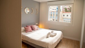 A bedroom with a bed, a window with a view of buildings, and a radiator. - Cozy Loriga (Vigo)