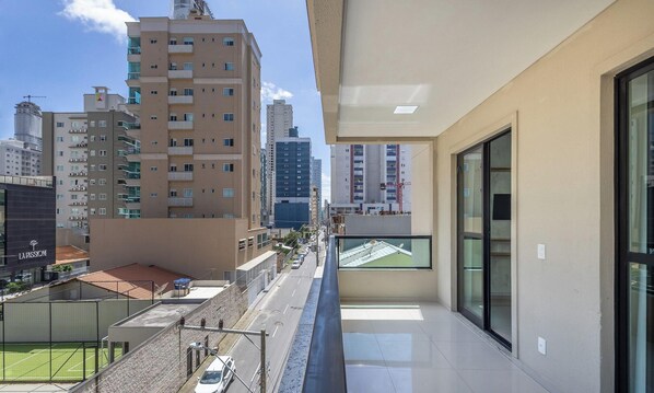 Un immeuble de grande hauteur, doté de nombreux étages et de balcons, une rue avec des voitures, et un court de tennis visible au premier plan.