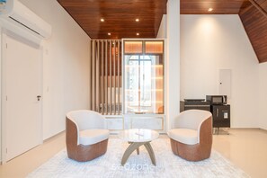Ein modernes Zimmer mit zwei Sofas, einem kleinen runden Tisch, einem fest eingebauten Fernseher und einer Schiebetür aus Glas zum Balkon.