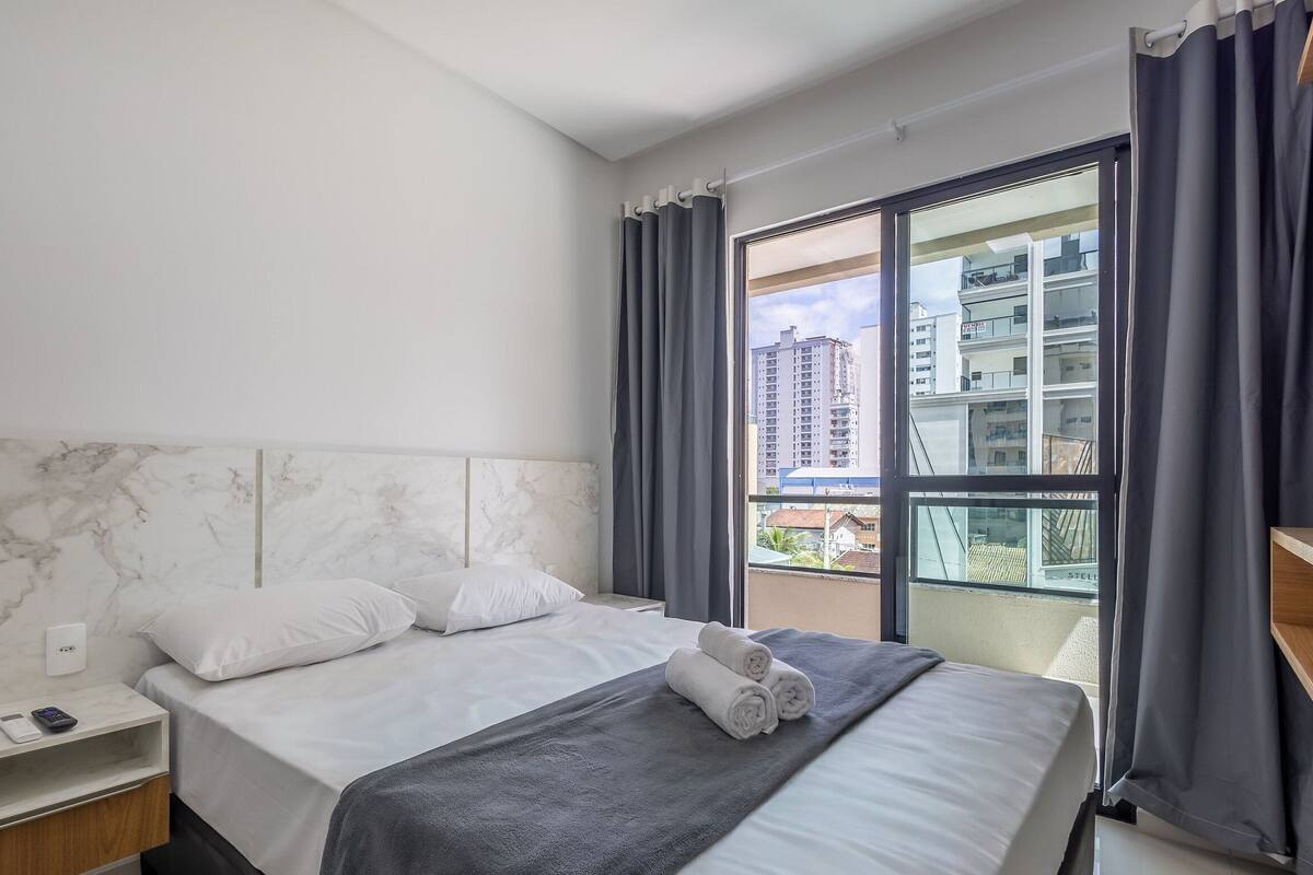 Ein Hotelzimmer mit Marmorkopfbrett, einem Bett mit weißer Bettwäsche, einer grauen Decke und Blick auf Gebäude durch ein großes Fenster.