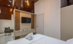 Une chambre d’hôtel moderne avec un plafond en bois, un téléviseur à écran plat fixé au mur, un minibar, un lit avec une serviette roulée et une chaise.