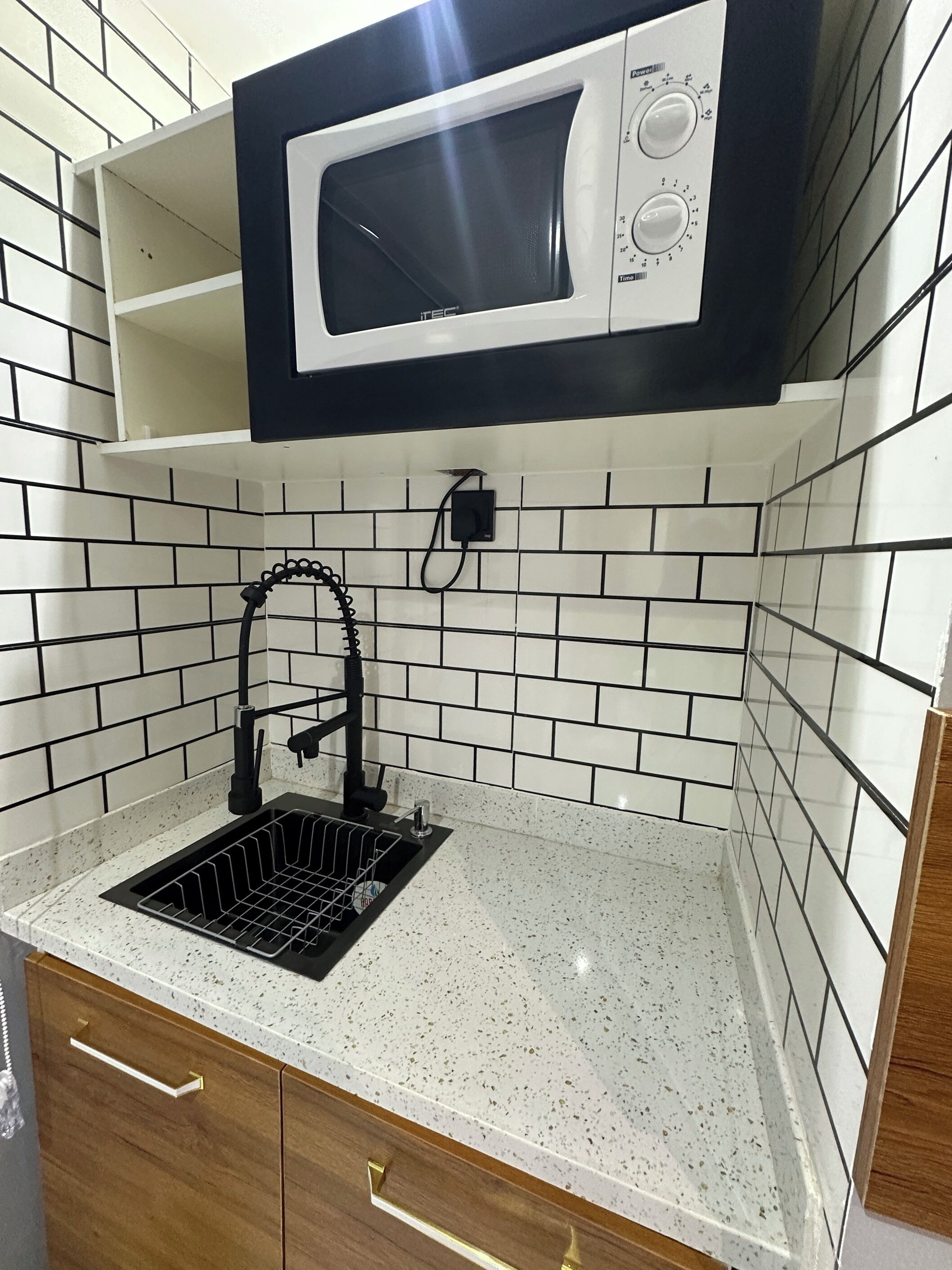 A kitchen with a black and white microwave, a stainless steel sink, and a tiled backsplash.