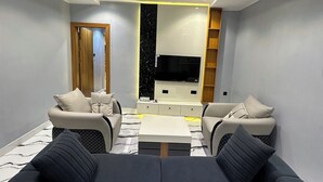 Ein modernes Wohnzimmer mit einer schwarzen Couch, zwei Sesseln, einem Couchtisch und einem Fernseher.