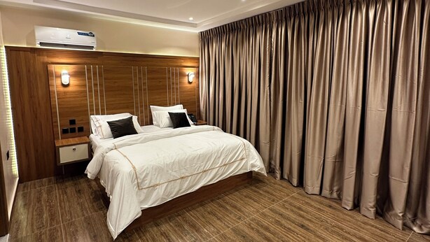 Ein modernes Schlafzimmer mit einem großen Bett, Holzvertäfelung, einer eingebauten Klimaanlage und einem fensterbedeckenden Vorhang.