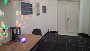 A room with a wooden table, a coffee maker, a chair, a door, and a tiled floor. - Espace Zen Bellevue (Sainte-Rose)