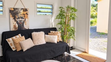 Una sala moderna con un sofá negro, almohadones decorativos, un cuadro grande, una planta de bambú y vistas a través de un ventanal.