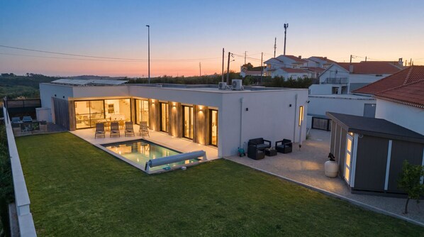 A modern house with a swimming pool, outdoor seating, and a well-maintained lawn.