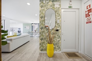 A modern interior with a white sofa, a yellow vase with sticks, a mirror, and a door with emergency exit signs.