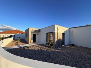 A modern house with a minimalist design, featuring a flat roof, large windows, and a gravel driveway.