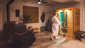 A person in a white robe opening a wooden sauna door with a Wellness Den logo. - Lakefront Spa Luxe • Theater & Game & View • USAFA 10 Min • Sleeps 10 (Monument)