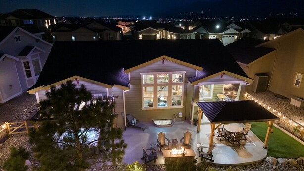 A residential house with a patio, outdoor seating, and a well-lit backyard. - Lakefront Spa Luxe • Theater & Game & View • USAFA 10 Min • Sleeps 10 (Monument)