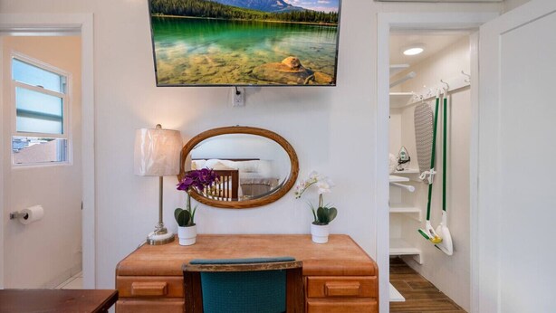 Quarto com escrivaninha de madeira, espelho, televisão acima da escrivaninha e vista para um lago pela janela.