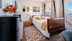 Quarto com cama, escrivaninha, cadeira, ventoinha no teto e janela com cortinas.