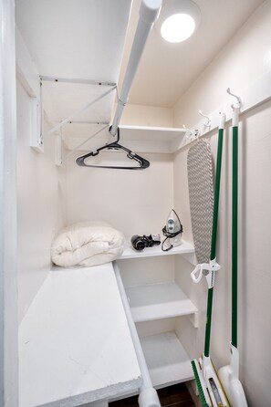 A compact, white utility room with a hanging clothes rack, a shelf with an iron and a hairdryer, and a green broom. - Chic & Stylish Studio Near Downtown LA * W/D * AC (Los Angeles)