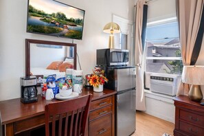 Une chambre d’hôtel compacte dotée d’une kitchenette, d’un coin repas et d’une grande fenêtre donnant sur un quartier résidentiel.
