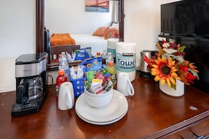 A hotel room with a coffee maker, a bowl of snacks, a bottle of Kirkland Premium Towels, and a vase of flowers on the table.