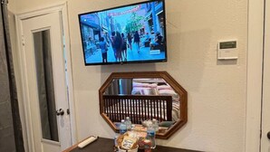 Ett hotellrum med ett skrivbord i trä, en tv som är monterad på väggen och ett litet bord med snacks och en vattenflaska.